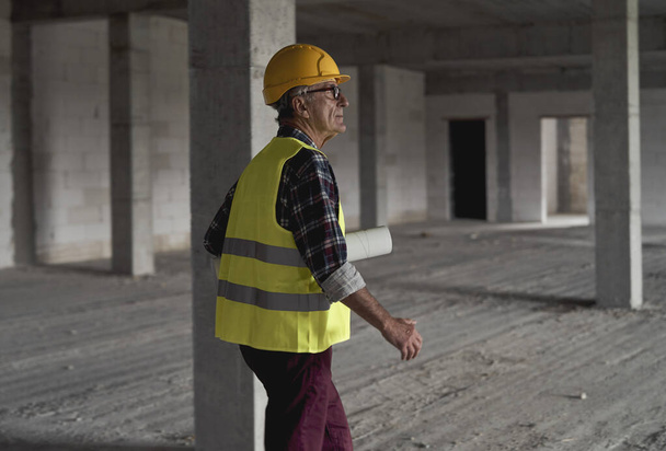 Hombre mayor caminando y sosteniendo planes en el sitio de construcción  - Foto, Imagen