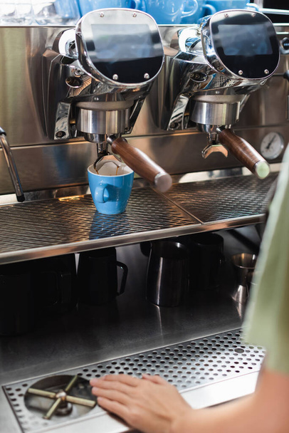 Обрізаний вид на бариста, що стоїть біля чашок і кавоварки в кафе
  - Фото, зображення