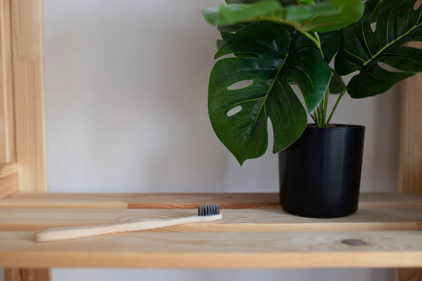 A stylish wooden toothbrush lies on a shelf next to a flower in a black pot. A wooden toothbrush lies on a wooden rack with a green flower. Selectiv focus - Foto, Bild