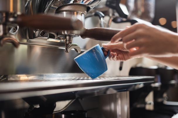 Vue recadrée de barista tenant tasse près de portafilter de la machine à café dans le café  - Photo, image