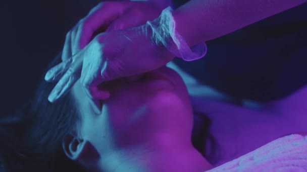 Vrouw massagist doet een gezichtsmassage met behulp van haar vingers op haar vrouwelijke cliënt - neon verlichting - Video