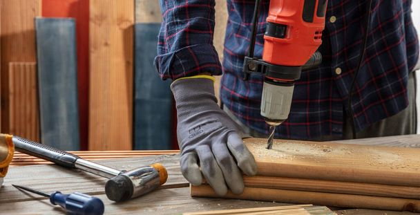 電動工具、大工手袋をはめた手掘削木製の板をドリル。建設業界,作業台の閉鎖ビュー - 写真・画像