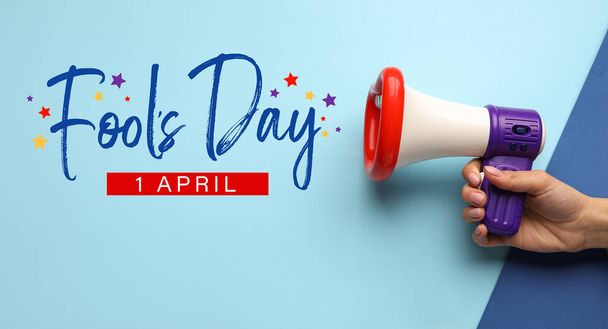 Female hand with funny megaphone on color background. April Fool's Day celebration - Photo, Image