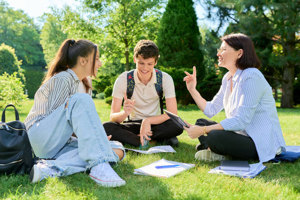 School teacher, psychologist, social worker talking to teenagers, sitting on grass - Fotoğraf, Görsel