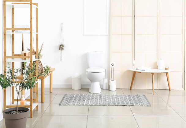 Интерьер светлого туалета с полками, комнатными растениями, унитазом, держателем бумаги и столом - Фото, изображение