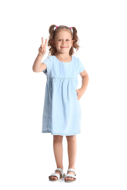 Funny little girl in blue dress showing victory gesture on white background - Foto, imagen