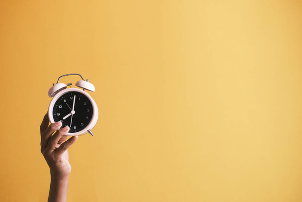  person hand holding alarm clock yellow background , - Fotoğraf, Görsel
