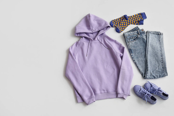 Elegante sudadera con capucha lila con calcetines, jeans y zapatillas de deporte sobre fondo claro - Foto, Imagen