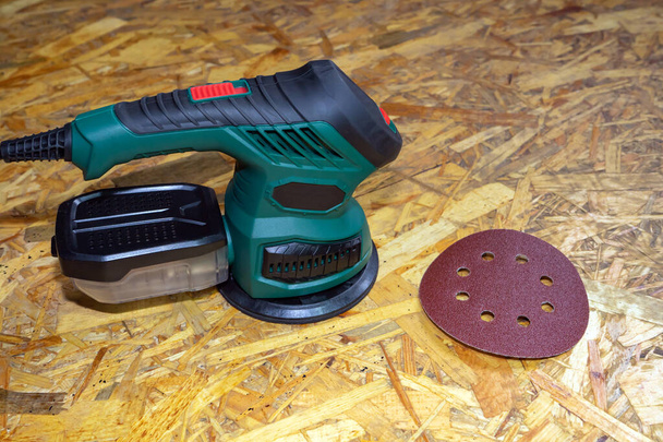 Eccentric orbital sander, grinder machine for wood and grinding wheel on a wooden surface, close up. - Photo, Image