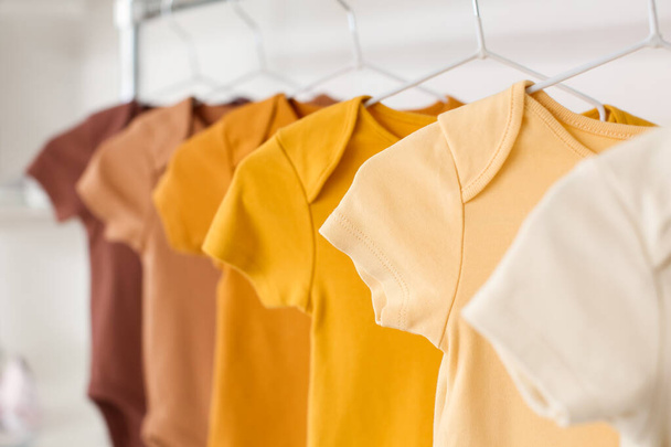 Baby bodysuits hanging near light wall in room, closeup - Photo, Image