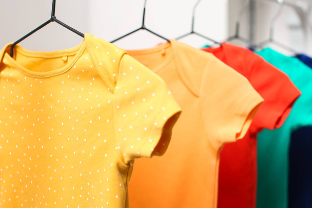 Kleurrijke baby bodysuits opknoping in lichte kinderkamer, close-up - Foto, afbeelding