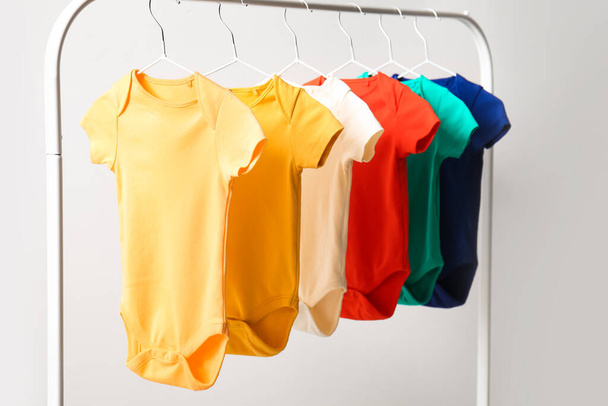 Rack met kleurrijke baby bodysuits in de buurt van lichte muur - Foto, afbeelding