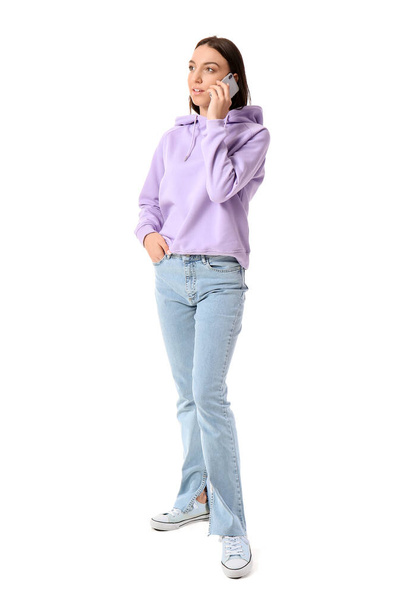 Pretty young woman in lilac hoodie talking by mobile phone on white background - Foto, Imagem