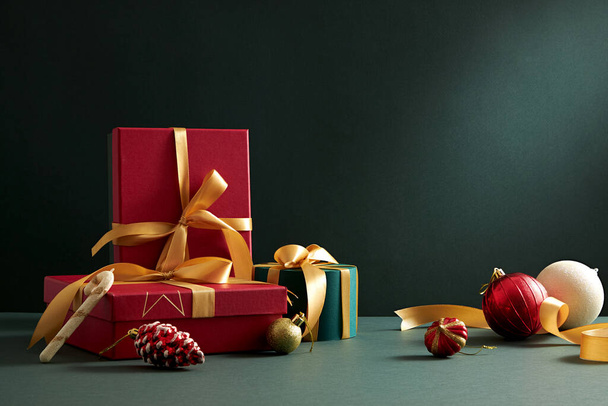 Coffret cadeau de Noël vert et rouge avec ruban jaune et ornement de Noël en arrière-plan vert avec espace vide pour la publicité, contenu de vacances photographie - Photo, image