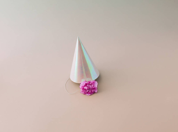Un sombrero de fiesta con una flor rosa debajo, sobre un fondo rosa. Concepto mínimo. - Foto, imagen