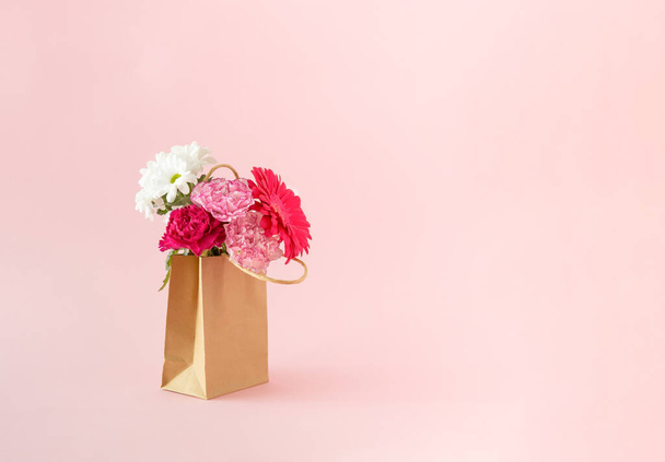 Tuoreita kukkia kukassa pakattu ruskeaan paperipussiin vaaleanpunaisella taustalla. Minimaalinen käsite. - Valokuva, kuva