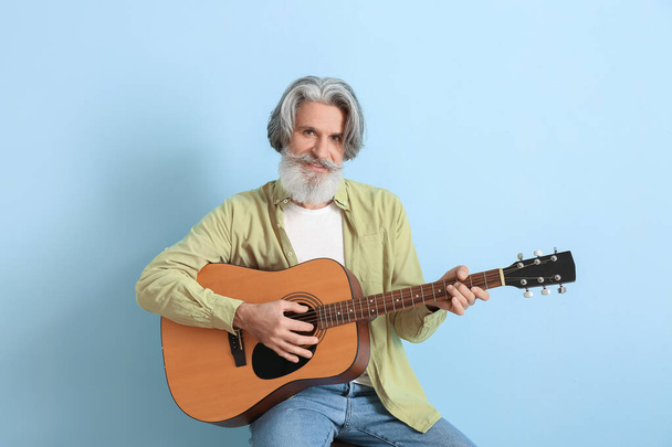 baard senior man spelen gitaar op blauwe achtergrond - Foto, afbeelding