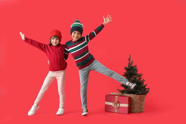 Happy little children in winter clothes, with Christmas tree and gift on color background - Photo, Image