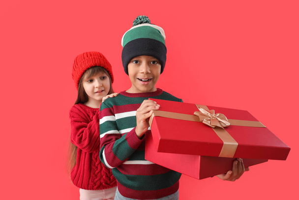 Cute little children in winter sweaters and with gift on color background - Photo, Image