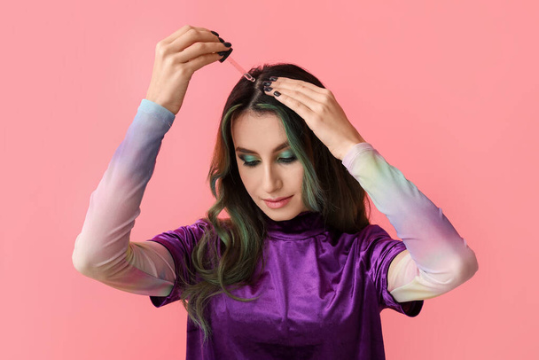 Mujer joven usando suero para el tratamiento de pérdida de cabello en el fondo de color - Foto, imagen