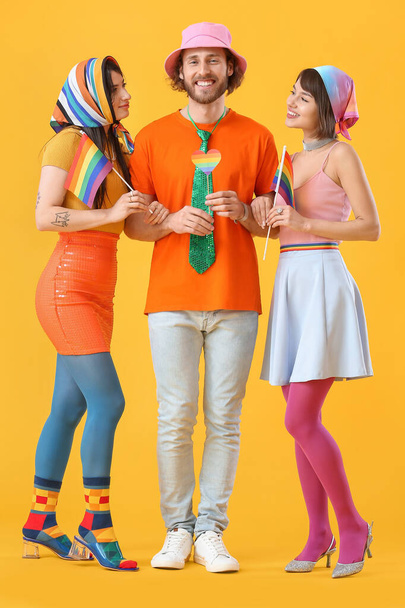 Man and two beautiful women in colorful clothes and with rainbow flags on color background. Concept of polyamory and LGBT - Photo, Image