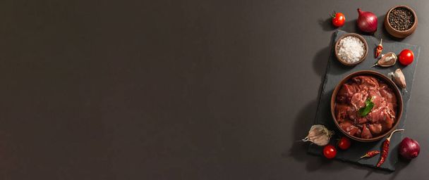 Hígado de pollo crudo en un tazón de cerámica. Ingrediente alimenticio fresco con especias. Luz dura de moda, sombra oscura. Fondo de hormigón de piedra negra, bandera - Foto, Imagen