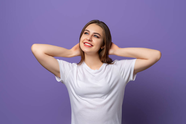 Portrait of dreaming brunette girl looking up with pleased face. Young woman relaxing, resting with hands behind head, carefree pose, purple background. - Photo, Image