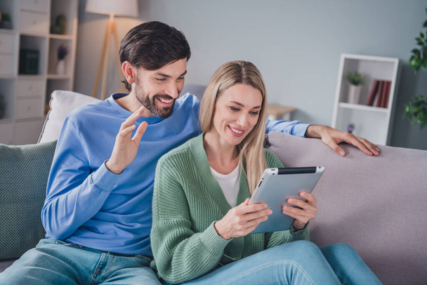 Portrait of two attractive cheerful people sitting on divan using device watching making video call waving hi hello at home indoors - Fotoğraf, Görsel
