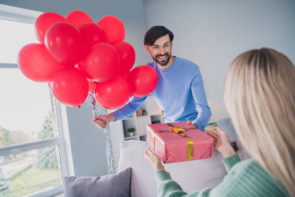 Photo of affectionate guy greet his lady spouse give giftbox packages hold red air balloons have romantic party in room apartment - Foto, Imagem