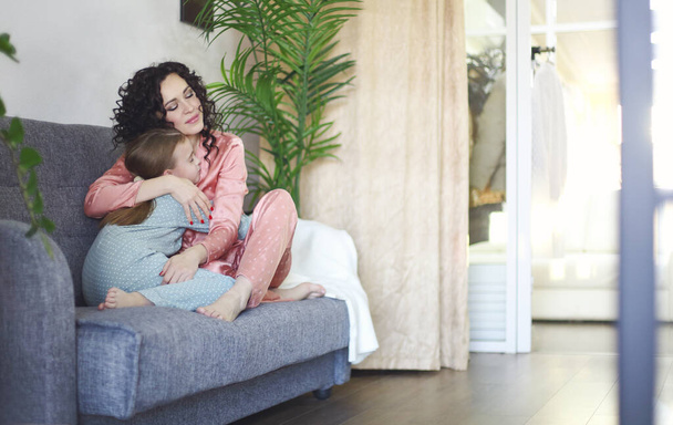 Hangulatos családi fotó boldog anya és lánya pizsamában pihentető kanapén reggel, fiatal gyönyörű anya és kislány gyermek töltik lusta családi hétvégén otthon. A család és az anyaság fogalma - Fotó, kép