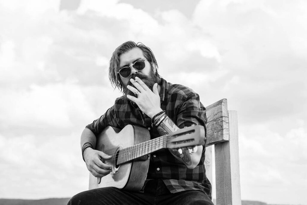 cigarette smoking. concept of music and vocal. man playing the acoustic guitar. brutal man with moustache and beard hold guitar. music shop. bearded man being a rock star. casual male guitarist - Fotografie, Obrázek
