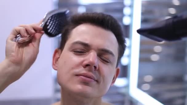 Giovane uomo pettinando e asciugandosi i capelli a bagno, facendo nuova acconciatura  - Filmati, video