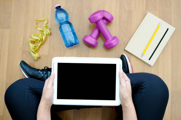 Frauen halten Tablets und blaue Kurzhantel-Trainingsgeräte und Wasserflaschen in der Hand, Notizbücher im Fitnessraum, Fitness- und Gesundheitskonzepte. - Foto, Bild