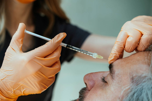 An Anonymous Doctor Injecting Botox on Man Face for Anti Aging Treatment at Medical Clinic. Close up photo of dermatologist hands makes rejuvenating biorevitalization facial injections procedure on mature male skin. - Foto, Bild