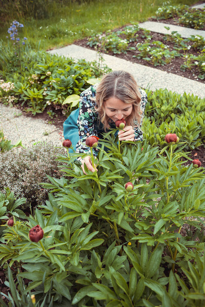 pretty blonde gardener working in garden with flowers and wearing green work apron - Foto, afbeelding