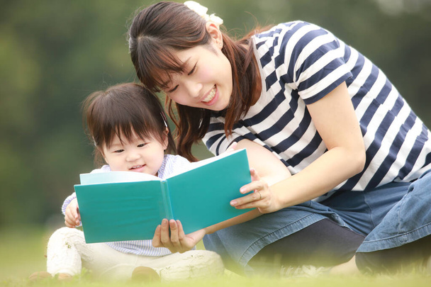 heureux mère et fille assis sur l'herbe et le livre de lecture - Photo, image