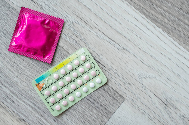 Pillole contraccettive e preservativi sul pavimento in legno. Concetto di oggetti o dispositivi anticoncezionali utilizzati per prevenire la gravidanza. - Foto, immagini