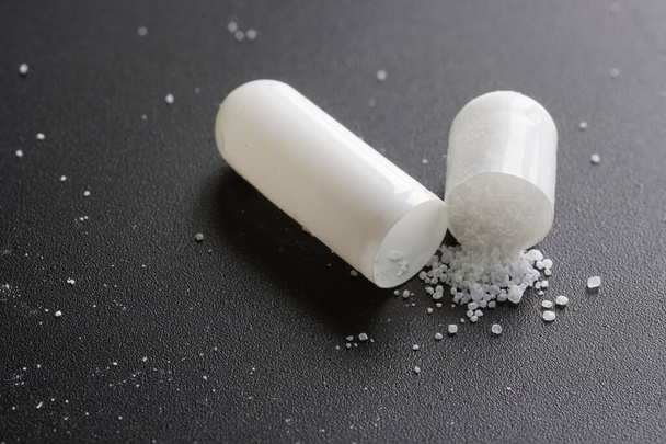 capsula pillola medica aperta con polvere bianca su uno sfondo nero strutturato. Macro. Concentrazione selettiva. Primo piano - Foto, immagini
