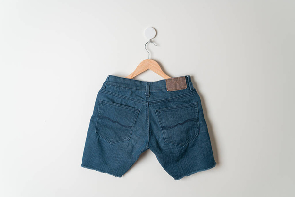 джинсы короткие, висящие на деревянной вешалке на стене - Фото, изображение