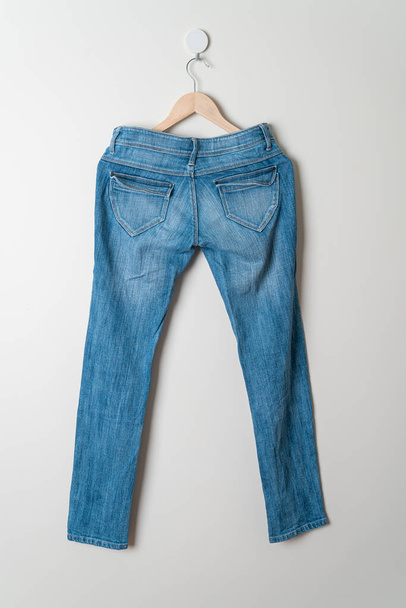 jeans trousers hanging with wood hanger on wall - Fotó, kép