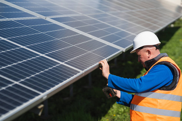 Mężczyzna inżynier mocuje panele słoneczne do metalowej ramy za pomocą śrub i klucza elektrycznego - Zdjęcie, obraz