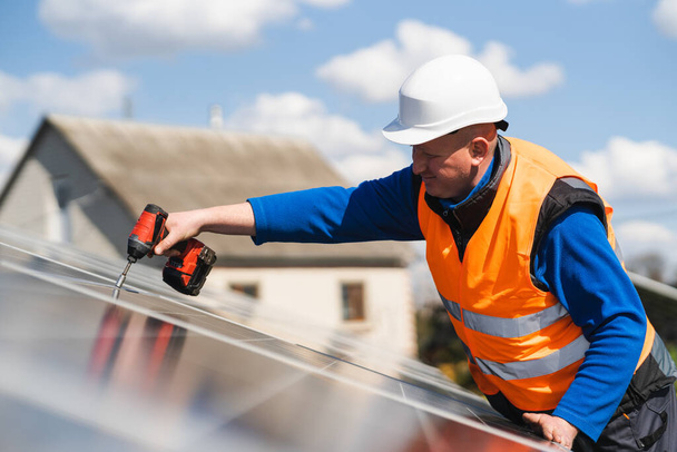 Man met boorschroevendraaier installeert panelen in een zonne-energiecentrale - Foto, afbeelding