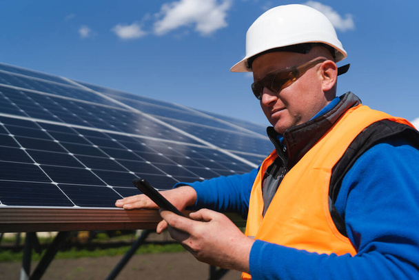 Homem de chapéu duro usando smartphone no fundo de painéis solares - Foto, Imagem