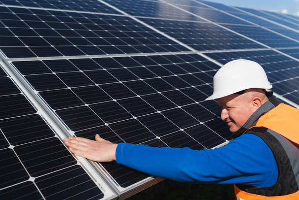 ハード帽子の太陽光発電所の労働者は、損傷のために彼の手で太陽光パネルの表面をチェックします - 写真・画像