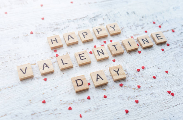 Feliz tarjeta de felicitación de San Valentín. Letras de madera sobre fondo blanco con pequeños corazones rojos dispersos.  - Foto, Imagen