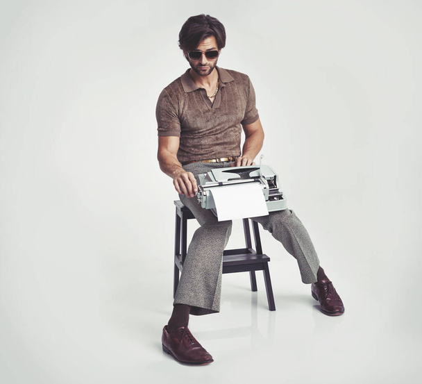 Who needs a desk anyway. A handsome man holding a retro typewriter and smoking a pipe while sitting on a stool. - Photo, image
