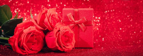 Punaiset ruusut ja lahjapakkaus kiiltävällä taustalla. Ystävänpäivä käsite, onnittelukortti. - Valokuva, kuva