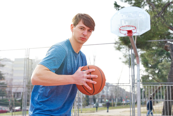 fiatal atléta edzés egy szabadtéri kosárpályán. kaukázusi férfi sportruházatban kosárlabdázik. - Fotó, kép