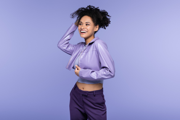 cheerful african american woman in violet leather jacket laughing isolated on purple - Foto, immagini