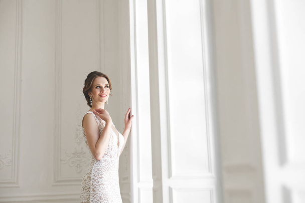 Beautiful bride posing in wedding dress in a white photo Studio. Mirror. Sofa. Bouquet. The door. Chandelier. - Φωτογραφία, εικόνα